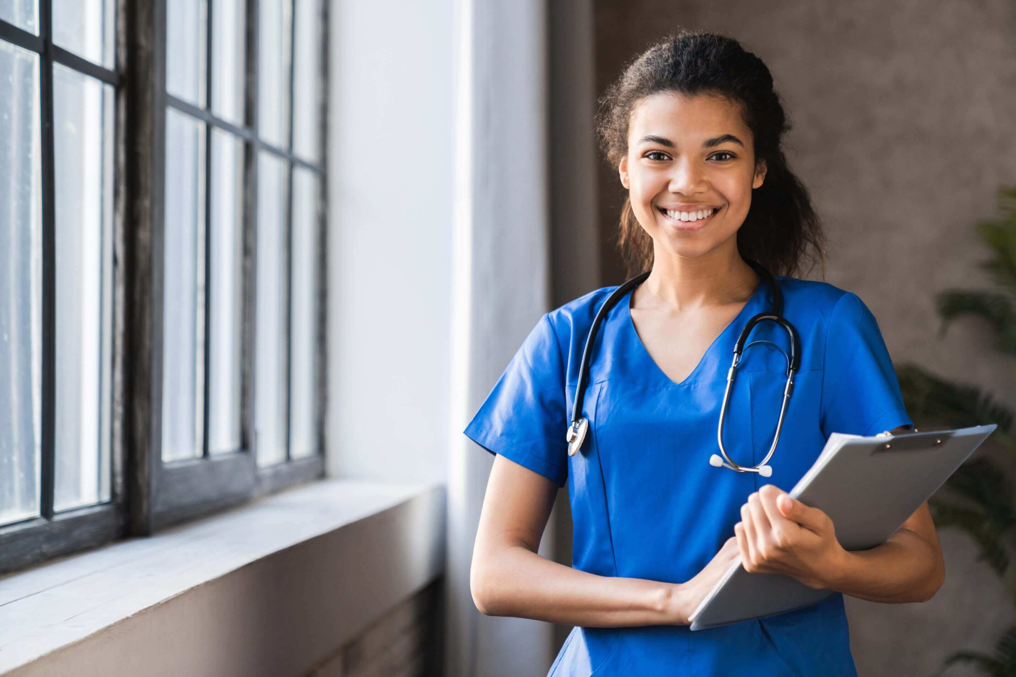 Smiling nurse holding a clipboard indoors.