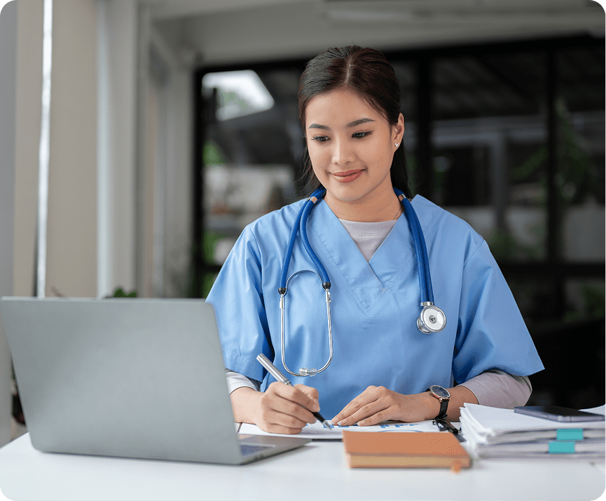 Doctor writing notes while using laptop.