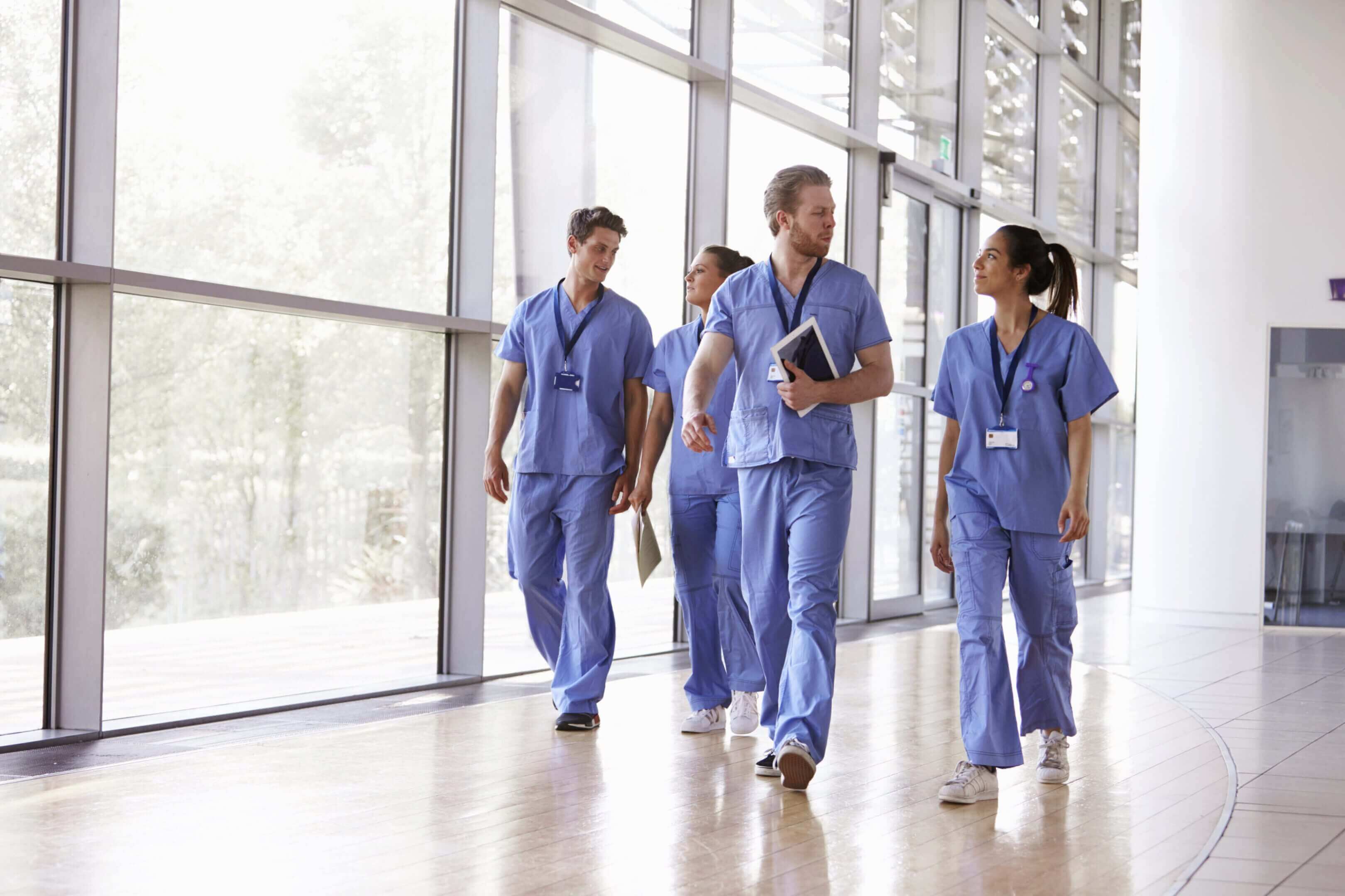 Three healthcare professionals walking and talking in a hospital corridor.