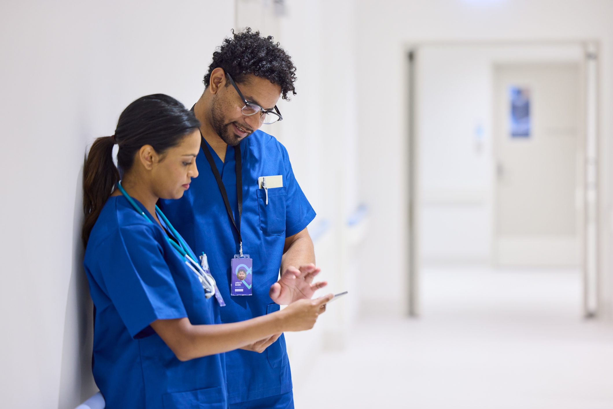 Two healthcare professionals in blue scrubs reviewing information in a hospital.