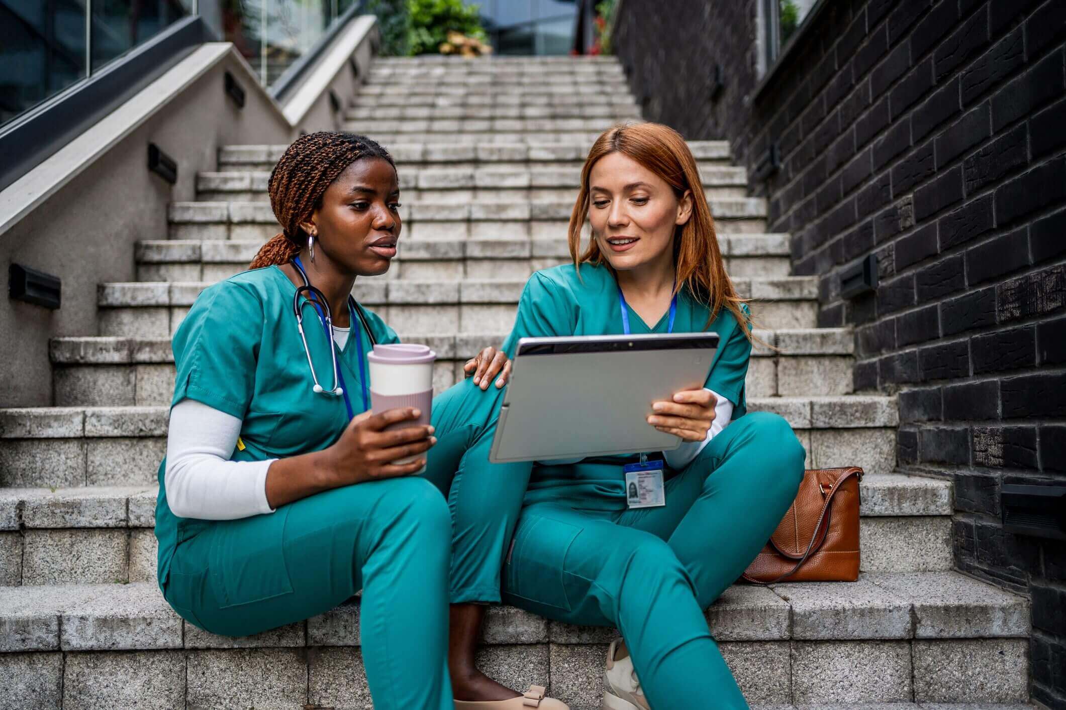 Two healthcare professionals reviewing medical information on a tablet outdoors.